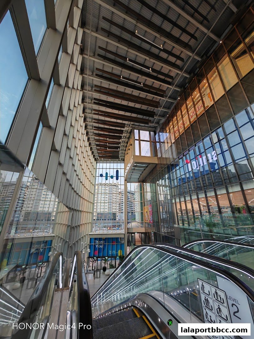 Modern interior of a shopping mall with escalators and large glass windows.