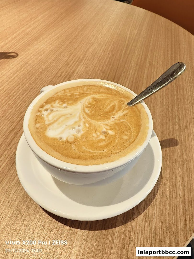 A close-up shot of a frothy latte with a spoon on a wooden table.