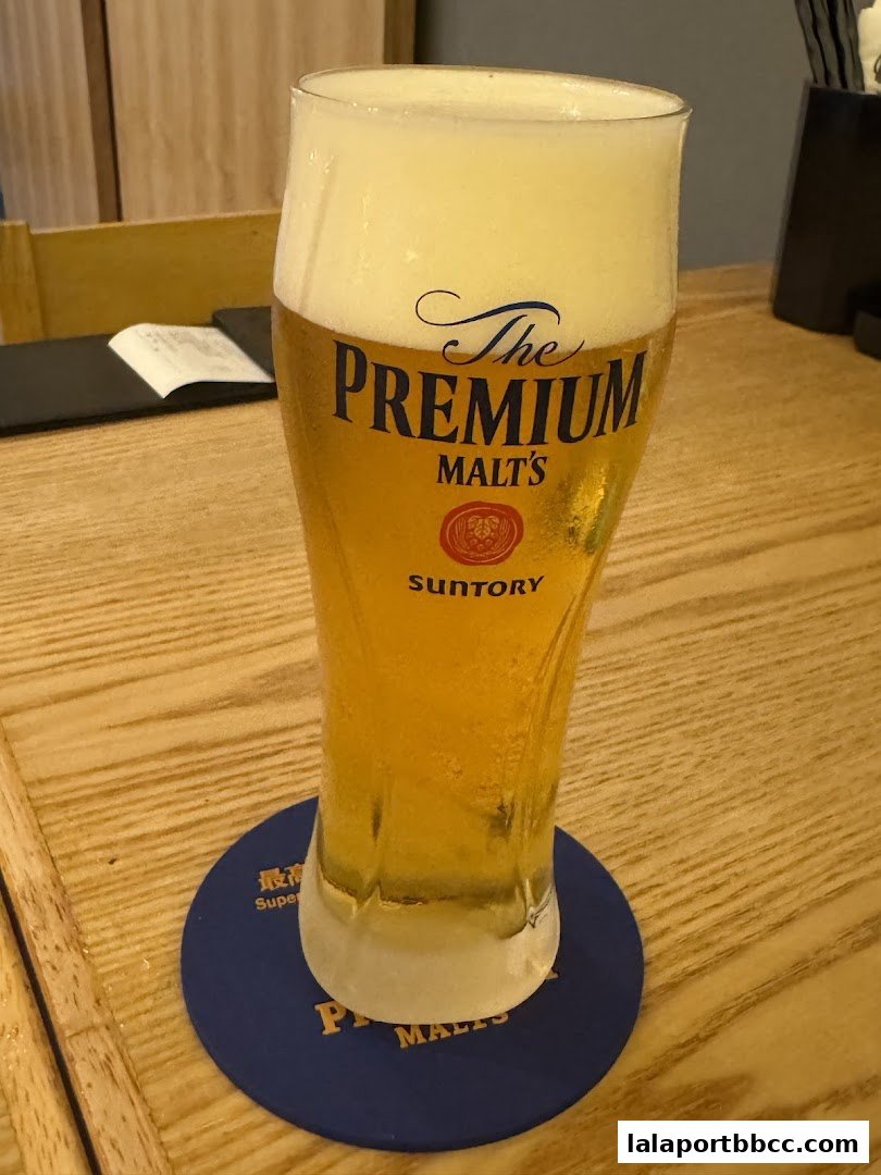 A tall glass of The Premium Malt's beer with a frothy head sits on a coaster.