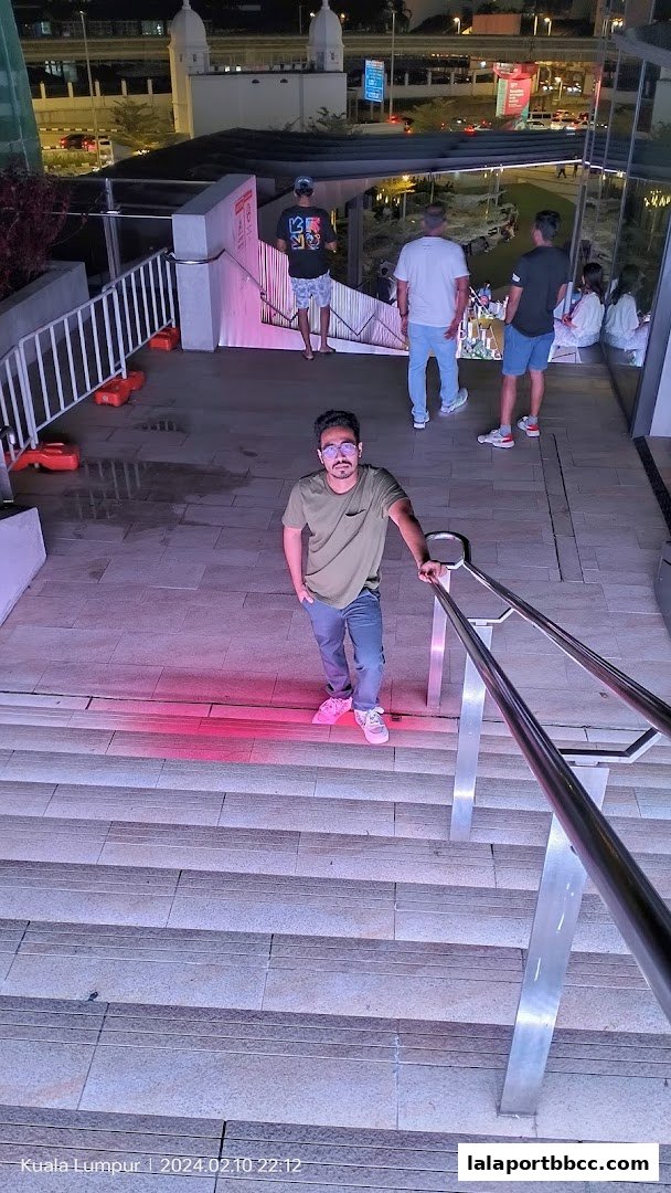 A man poses on illuminated steps at night with other people in the background.