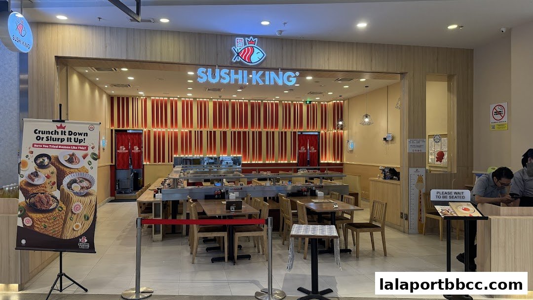 The exterior of Sushi King Lalaport BBCC, featuring a conveyor belt sushi setup and seating.