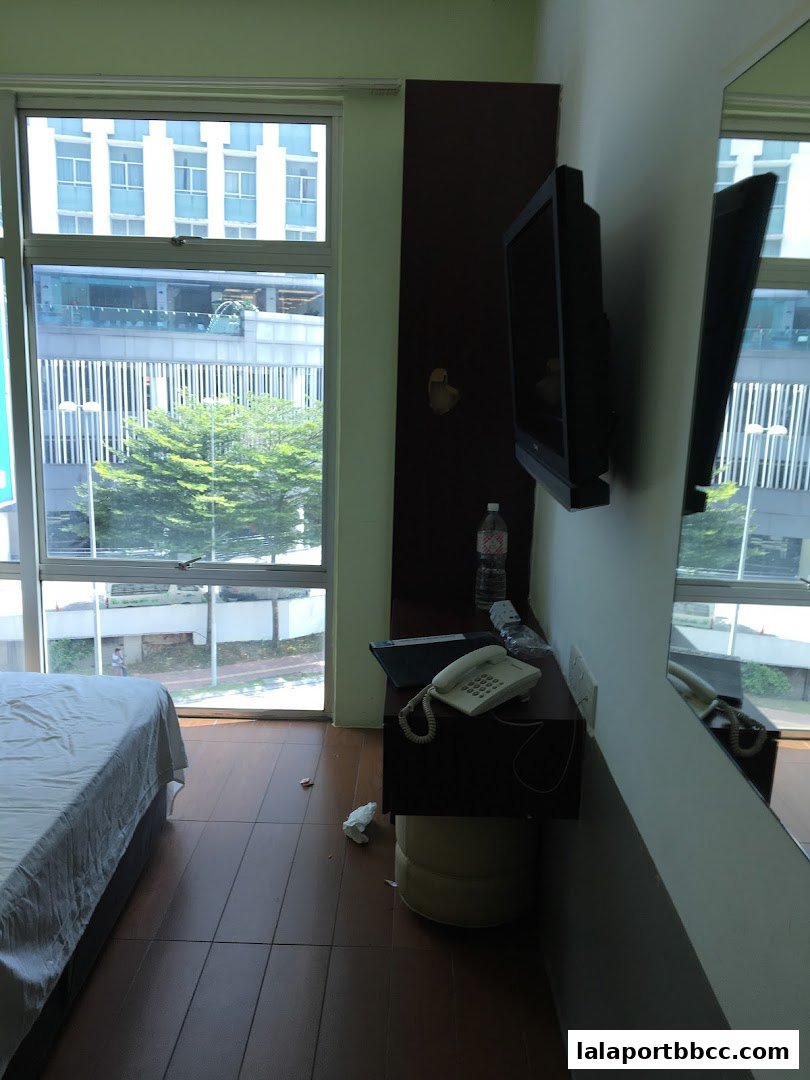 A hotel room with a bed, TV, telephone, and a large window overlooking a city.