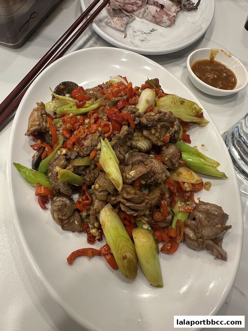 A plate of stir-fried meat with chili peppers and scallions, served with a side of dipping sauce.