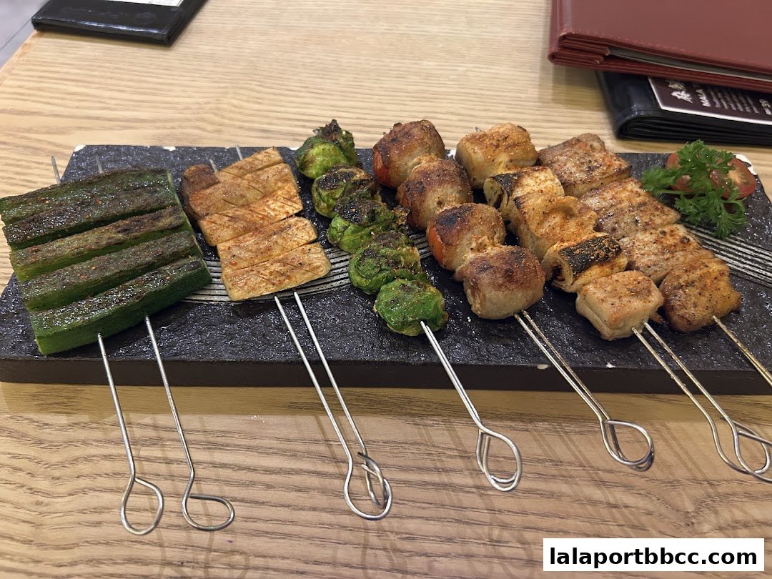 A platter of assorted grilled skewers, including okra, mushrooms, and meat, served on a dark stone plate.