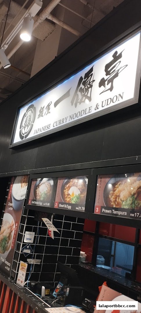 A food stall sign and menu display for Japanese curry noodles and udon.