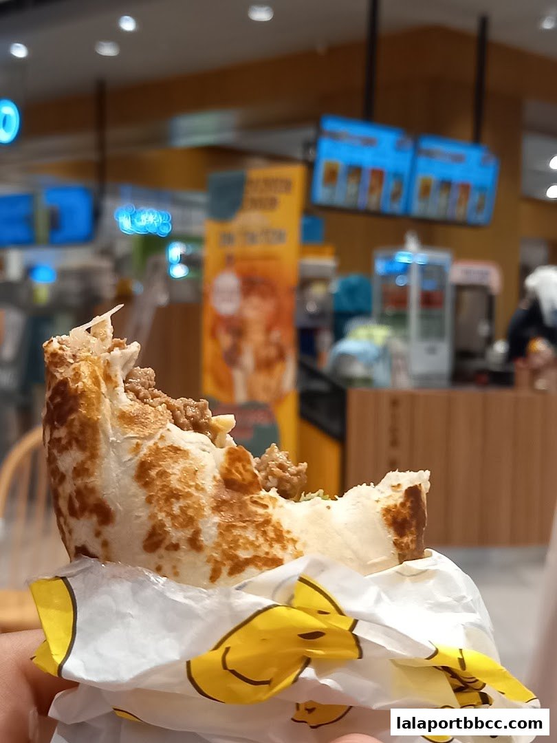 A close-up of a delicious kebab wrap being held, with the shop interior blurred in the background.