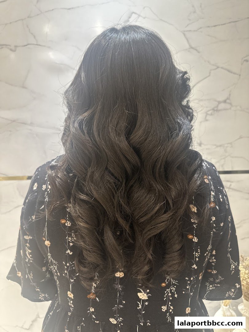 A person's back with beautifully styled, wavy dark hair against a marble background.