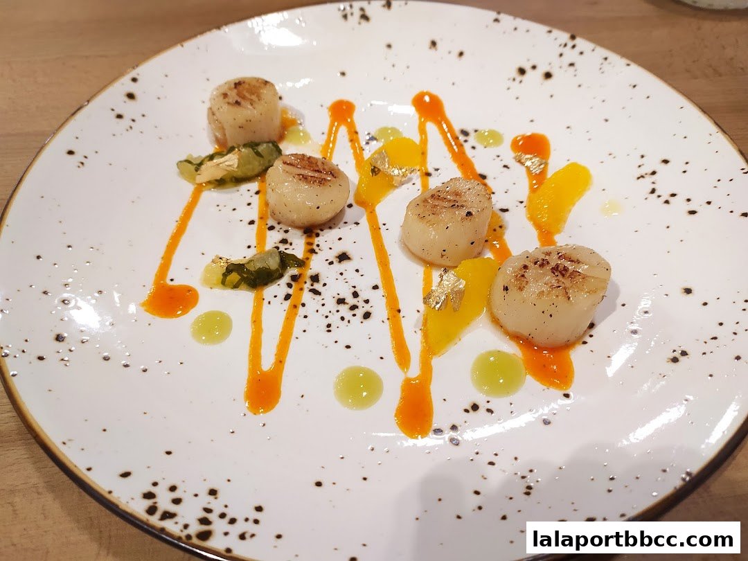 A plate of seared scallops with orange sauce, green puree, and gold leaf.