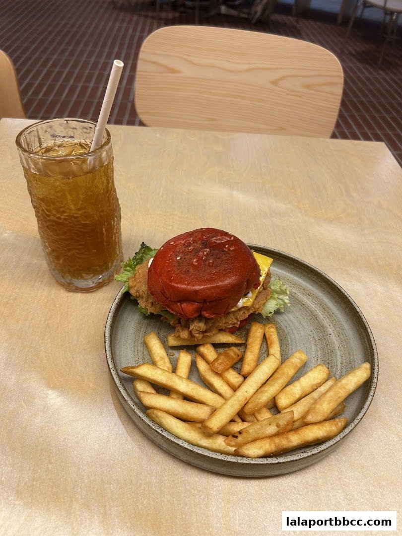 A red bun burger with fries and a drink on a wooden table.