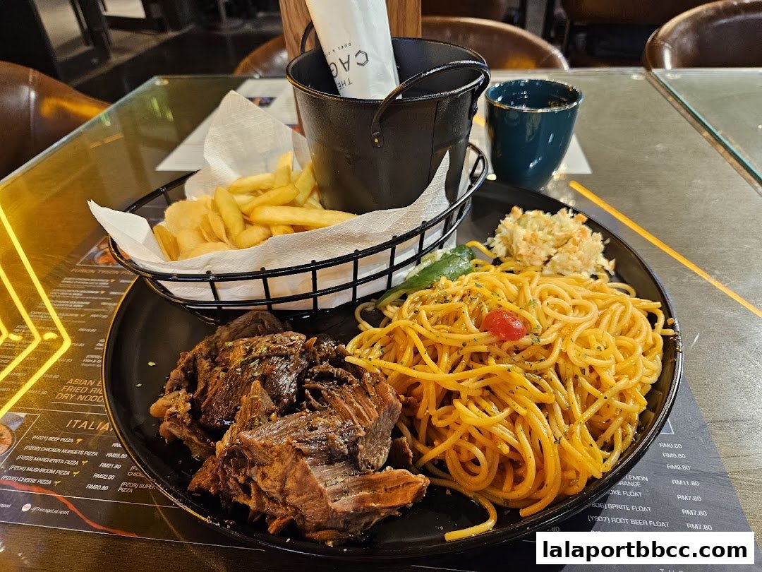 A plate of food with spaghetti, meat, fries, and coleslaw, served at The CAGE.