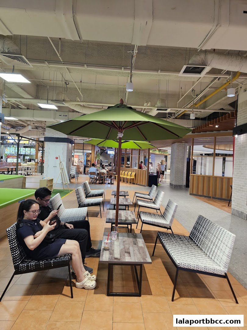 People relaxing at tables with umbrellas in a food court area.