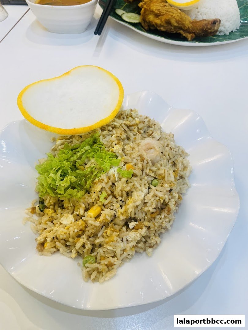 A plate of fried rice with a prawn and a side of crispy crackers, with another dish in the background.