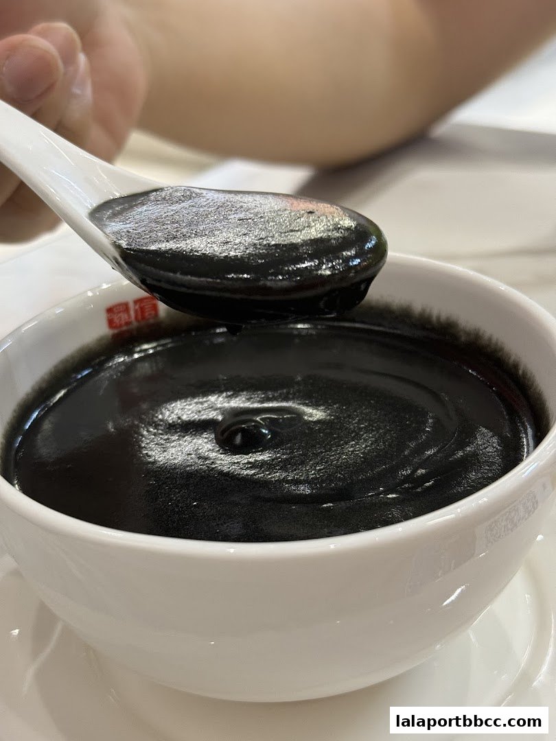 A close-up of a spoon scooping black sesame dessert from a white bowl.