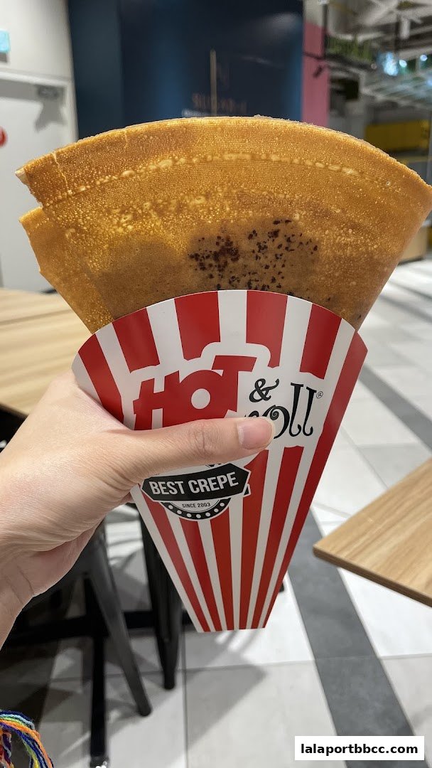 A hand holds a freshly made crepe in a branded red and white striped wrapper.