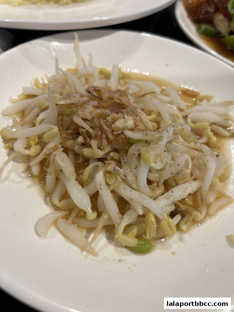 A close-up shot of a plate of bean sprouts with fried shallots and a savory sauce.