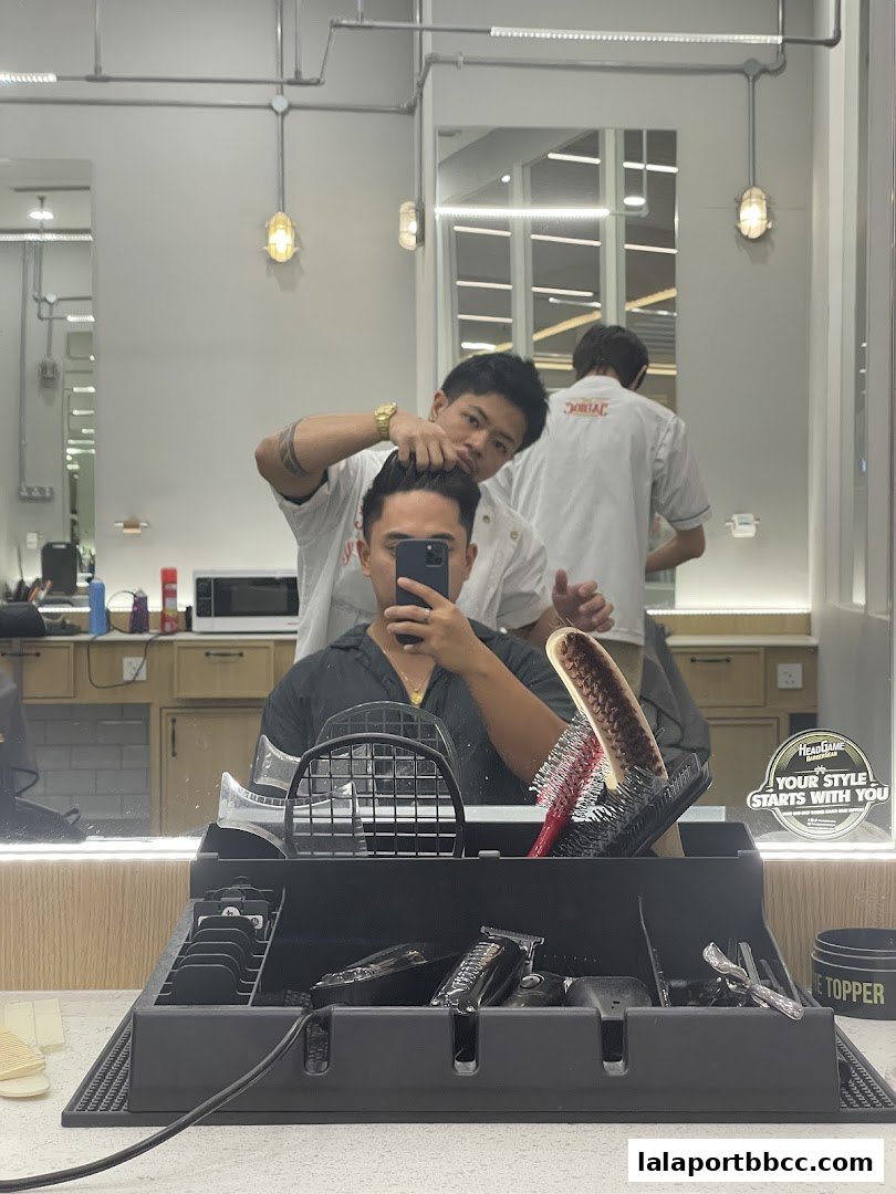 A barber is styling a customer's hair in a modern barbershop.