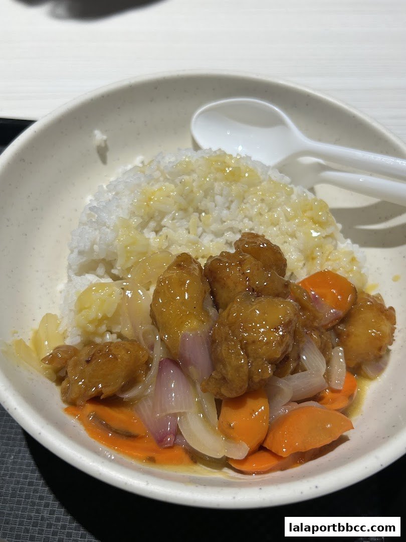 A bowl of fried rice topped with sweet and sour chicken, carrots, and onions.