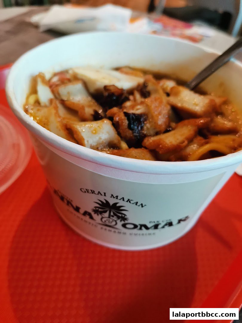 A close-up of a bowl of noodles with meat and egg, served in a takeaway container.