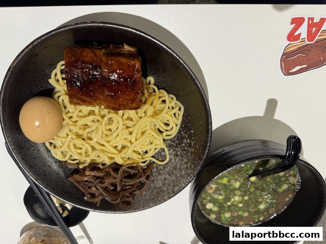 A bowl of ramen with noodles, braised pork, egg, and wood ear mushrooms, served with a side of broth.