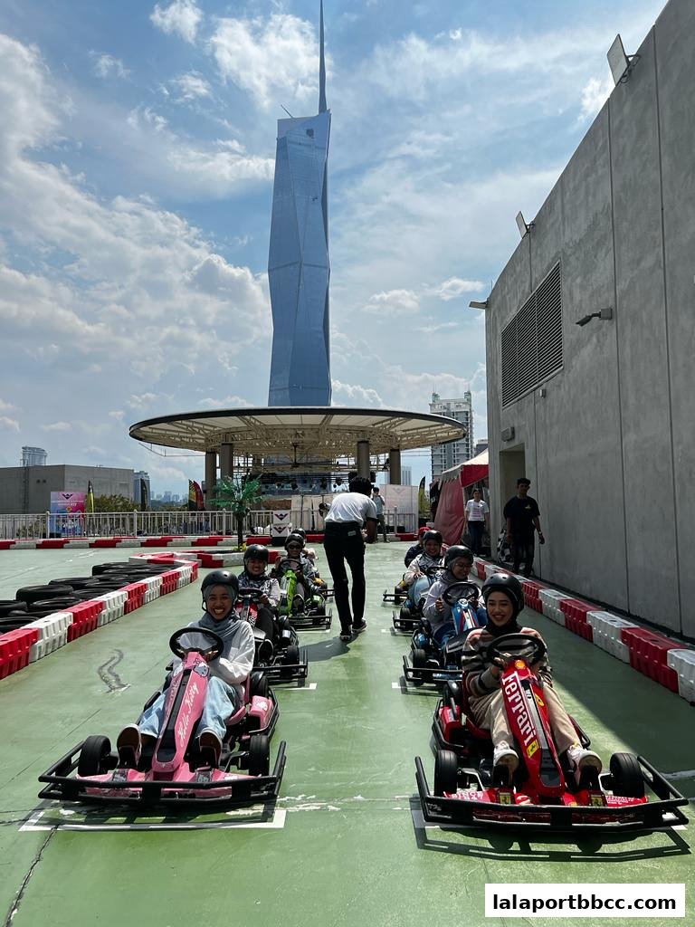 People enjoying go-karting on a sunny day with a distinctive skyscraper in the background.