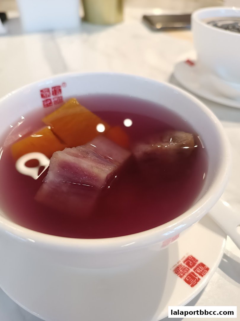 A close-up of a bowl of purple dessert soup with chunks of taro and sweet potato.
