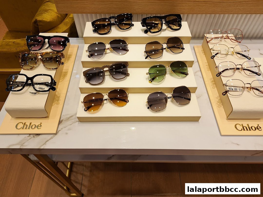 A display of various Chloe sunglasses and eyeglasses on white stands.