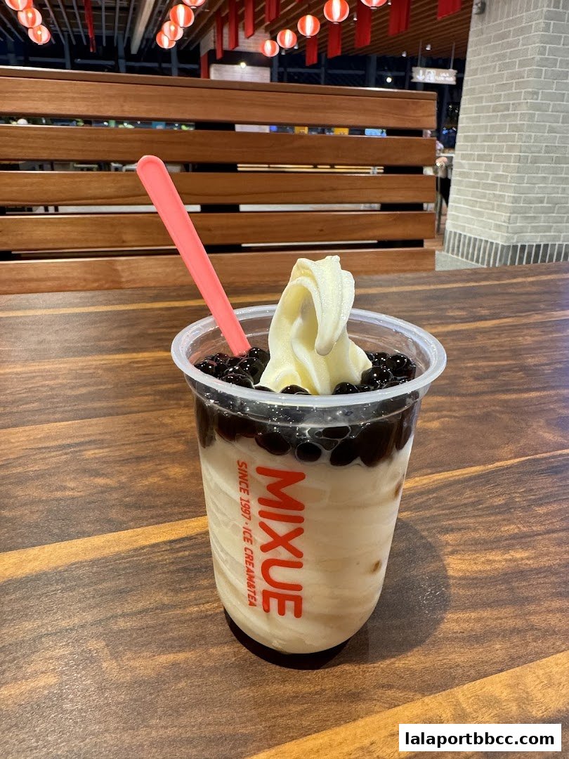 A creamy soft-serve ice cream with boba pearls and a pink spoon in a clear cup.