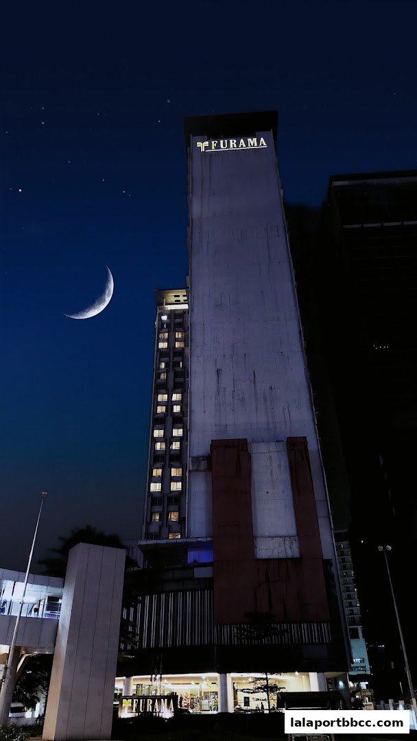 A tall building with the Furama logo illuminated at night, under a crescent moon.