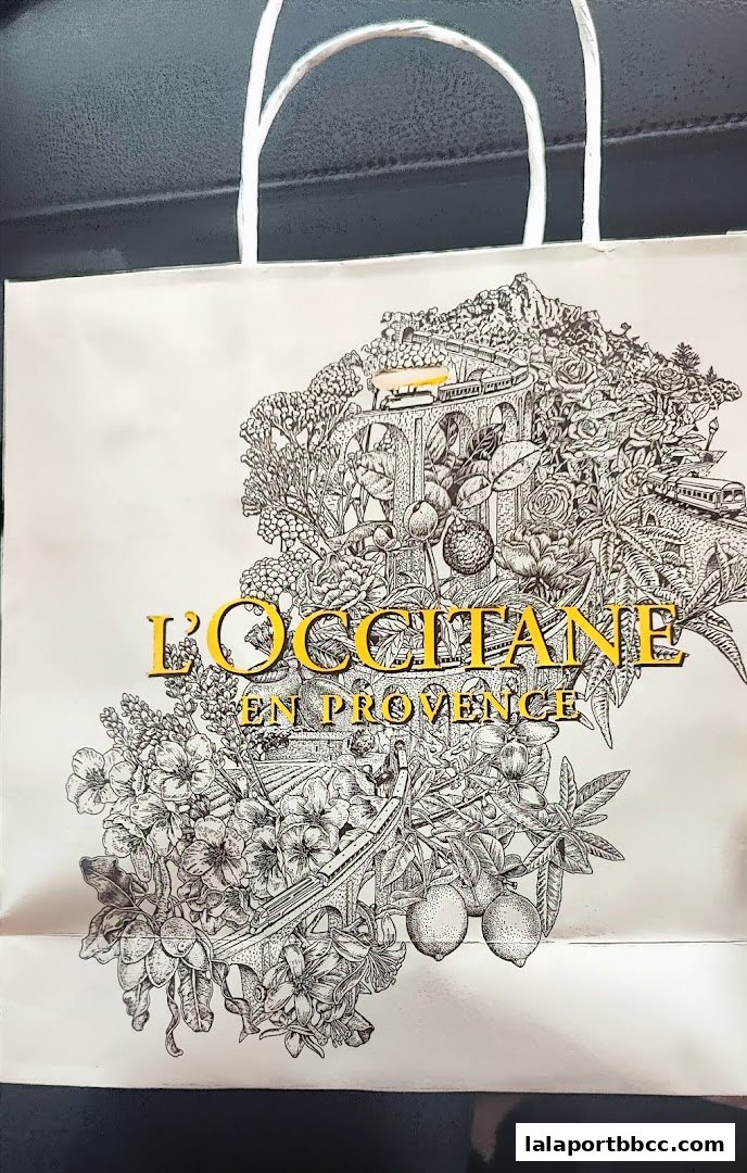A shopping bag from L'Occitane En Provence featuring intricate botanical illustrations and a scenic landscape.