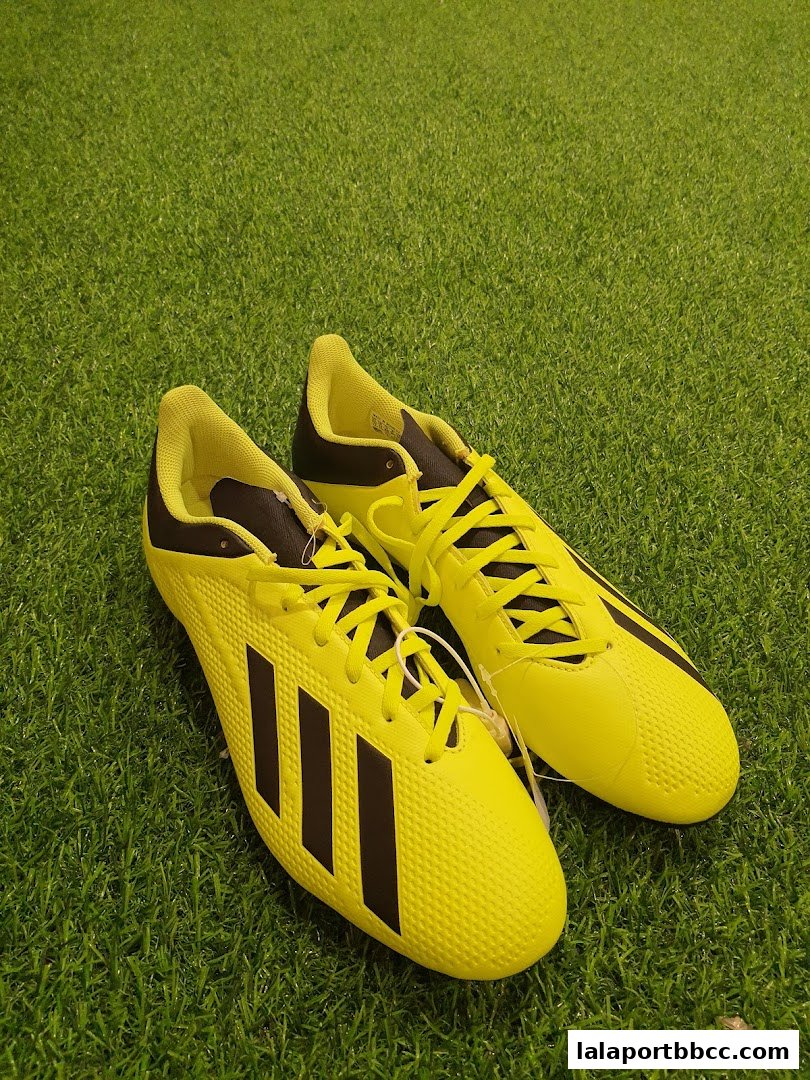 A pair of bright yellow Adidas soccer cleats with black stripes on a green grassy surface.