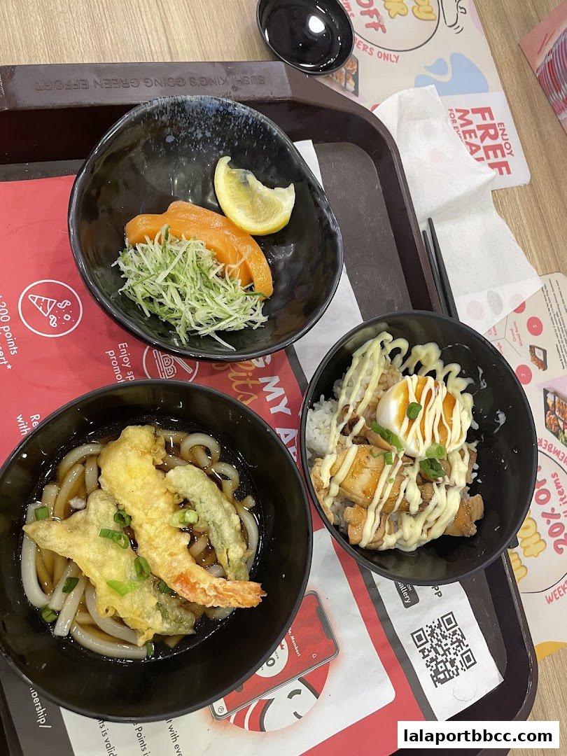 A tray with three bowls of Japanese food: salmon sashimi, udon noodles with tempura, and chicken teriyaki rice bowl.