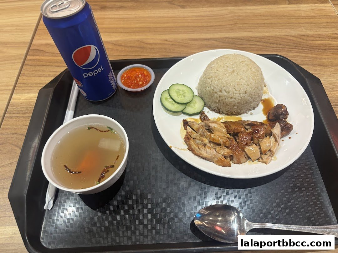 A tray of chicken rice with a Pepsi, soup, and chili sauce.