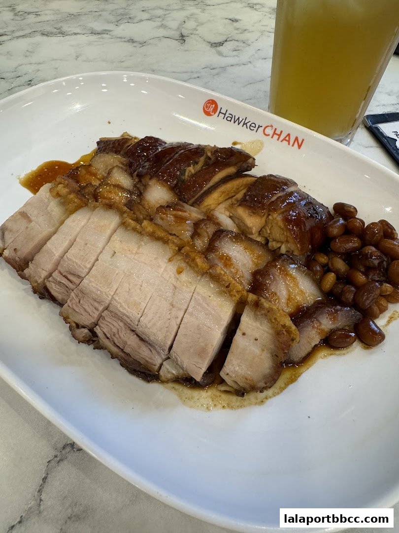 A plate of roasted meats, including crispy pork belly and char siu, with a side of peanuts and a drink.