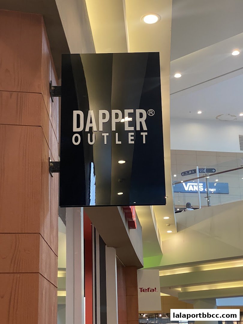 A sign for Dapper Outlet is displayed on a wooden pillar in a shopping mall.