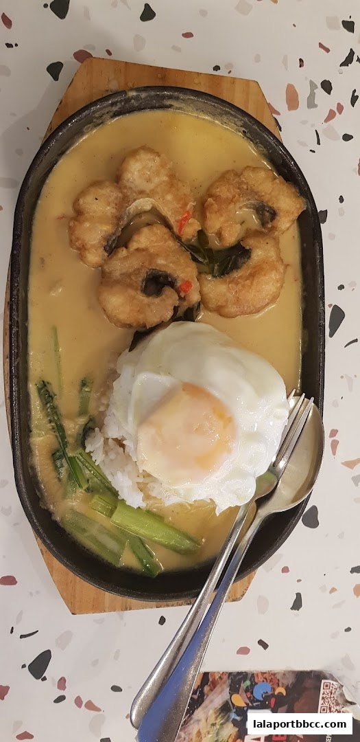 A sizzling claypot dish with fried fish, rice, and a fried egg, served with cutlery.