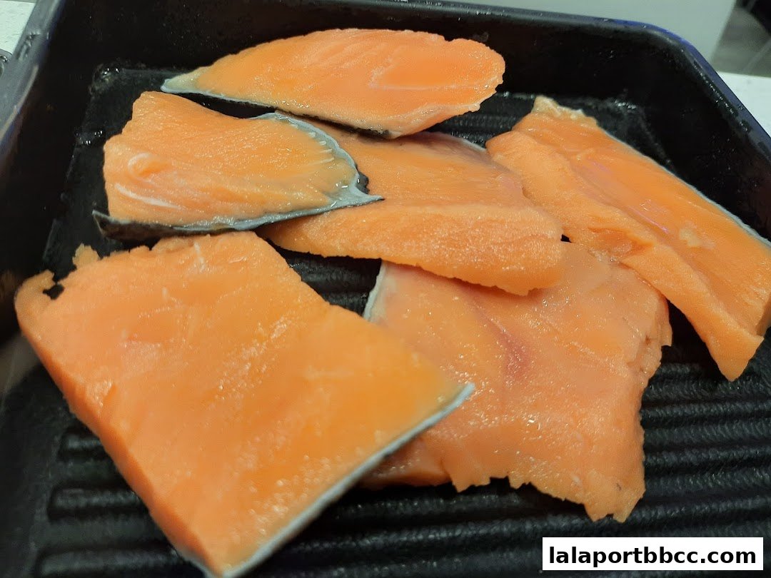 Fresh, raw salmon slices arranged in a black tray, ready for cooking.
