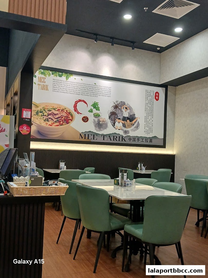 Interior of a restaurant with green chairs and tables, featuring a large mural about Mee Tarik.