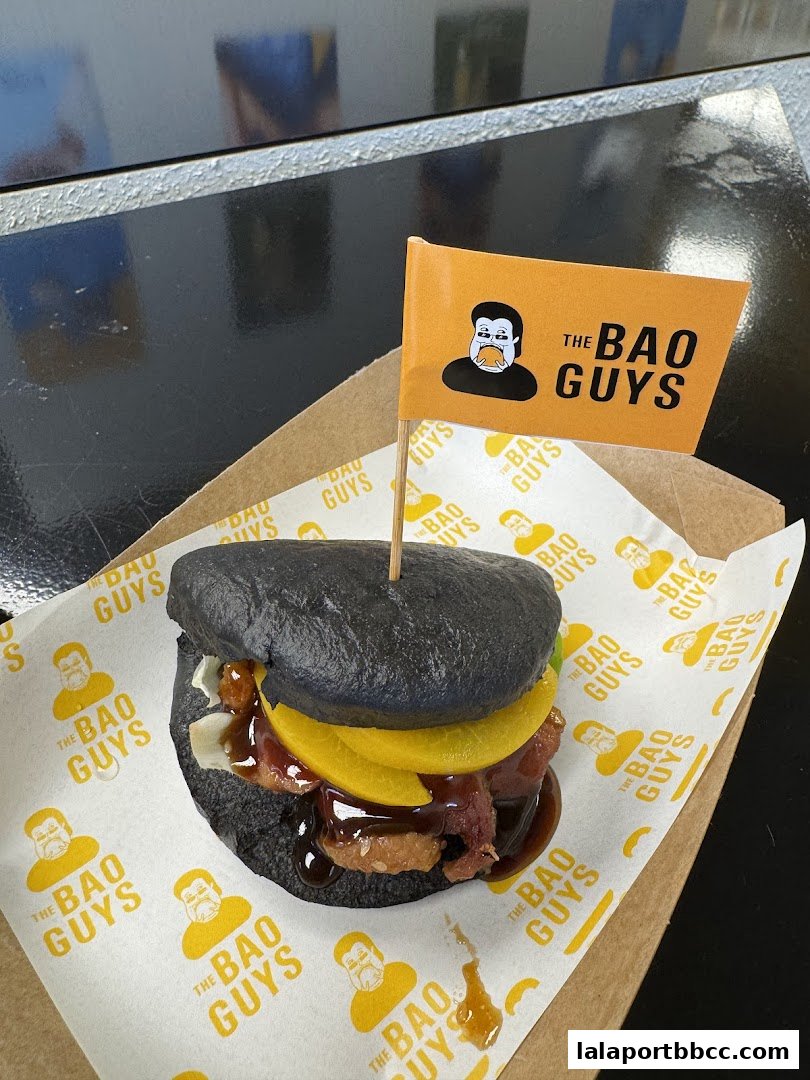 A close-up of a black bao bun sandwich with a flag from 'The Bao Guys'.