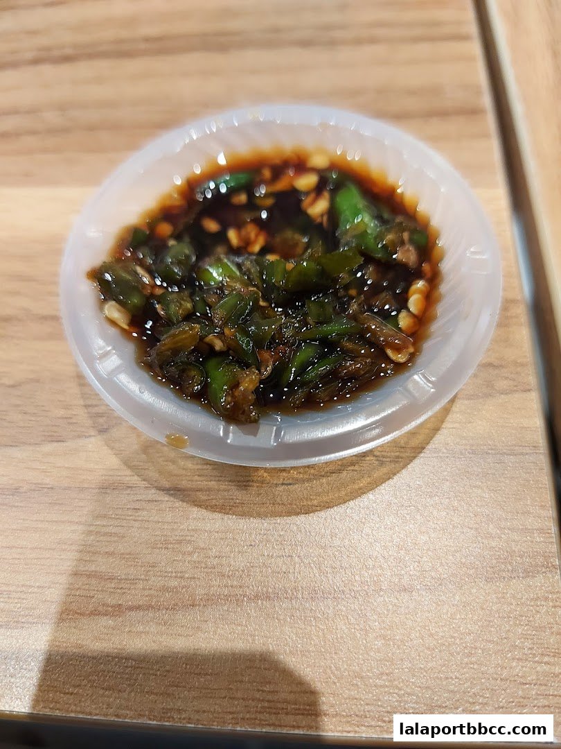 A close-up of a small dish containing chopped green chilies in a dark sauce.