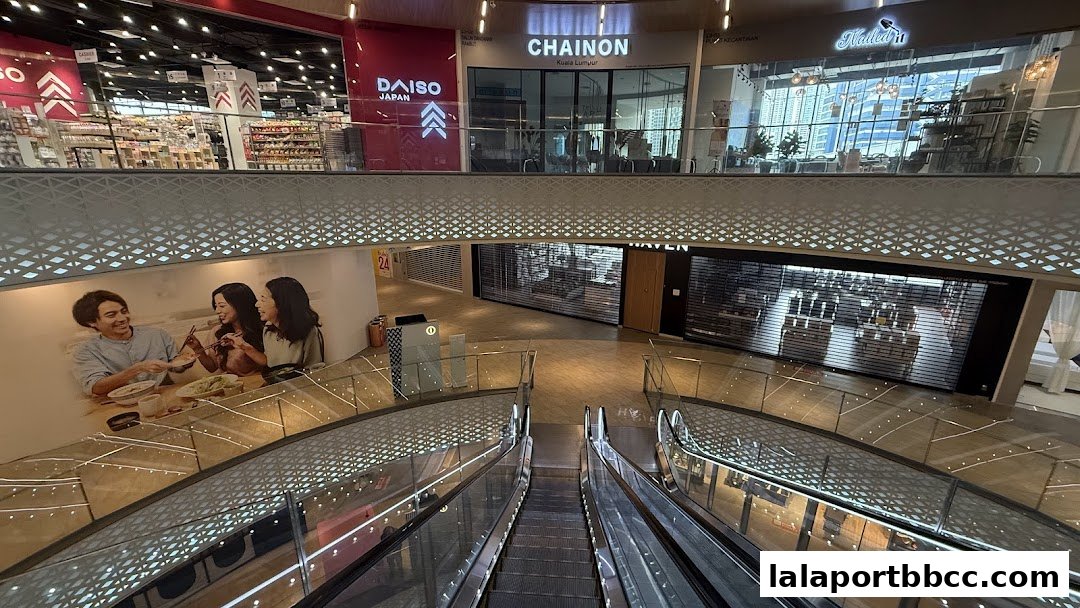 View of the DAISO Japan store and other shops from an escalator in a mall.
