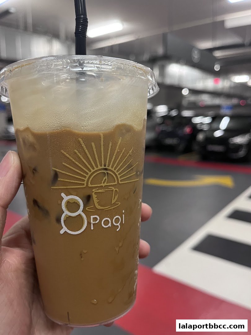 A hand holds a cold coffee drink with the '8 Pagi' logo on the cup.
