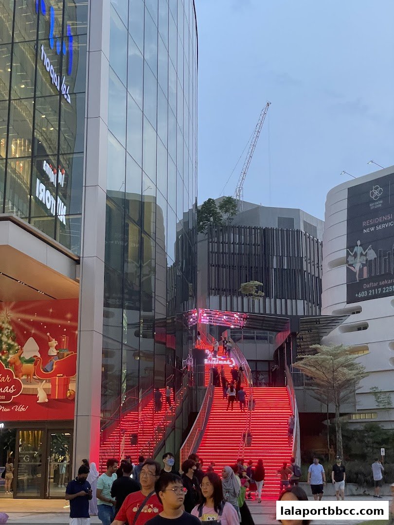 People walk up a brightly lit red staircase outside a modern building with glass facades.