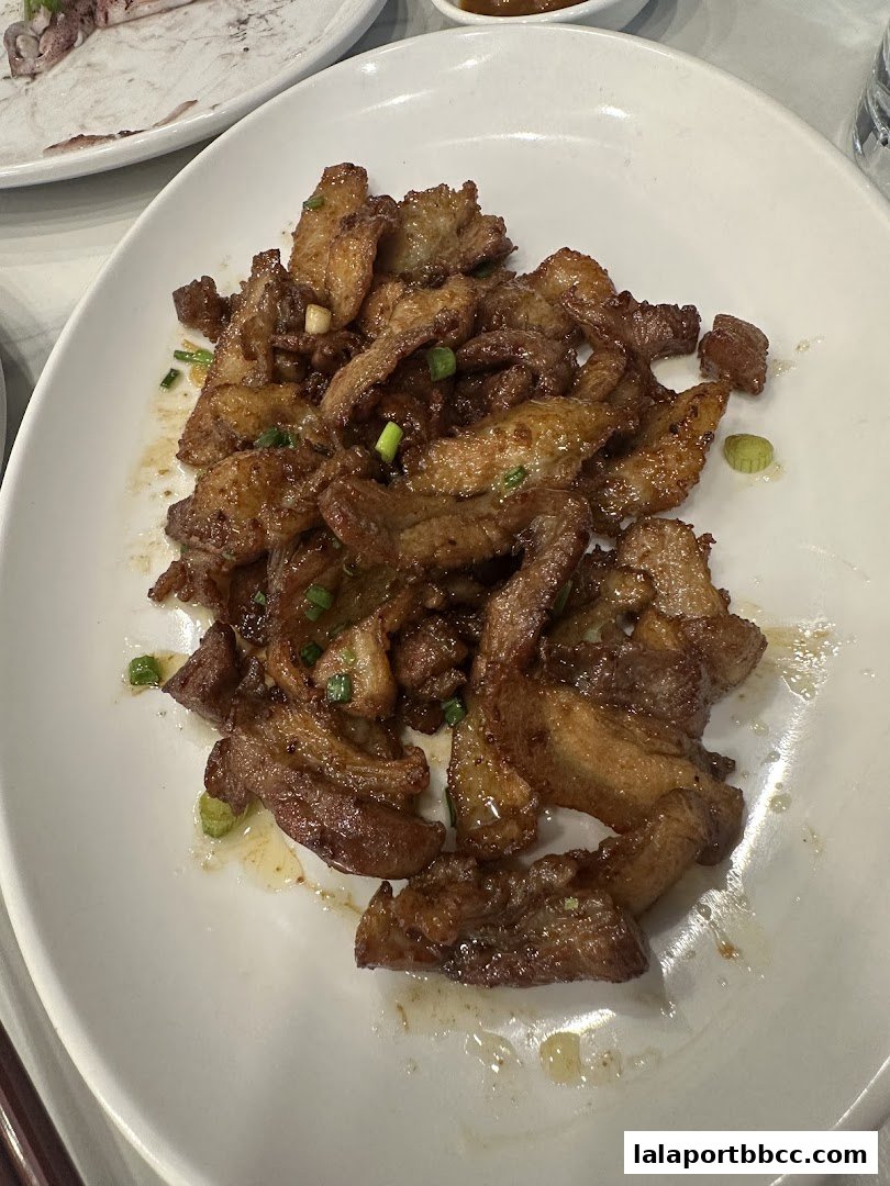 A plate of savory braised pork belly slices garnished with chopped scallions.