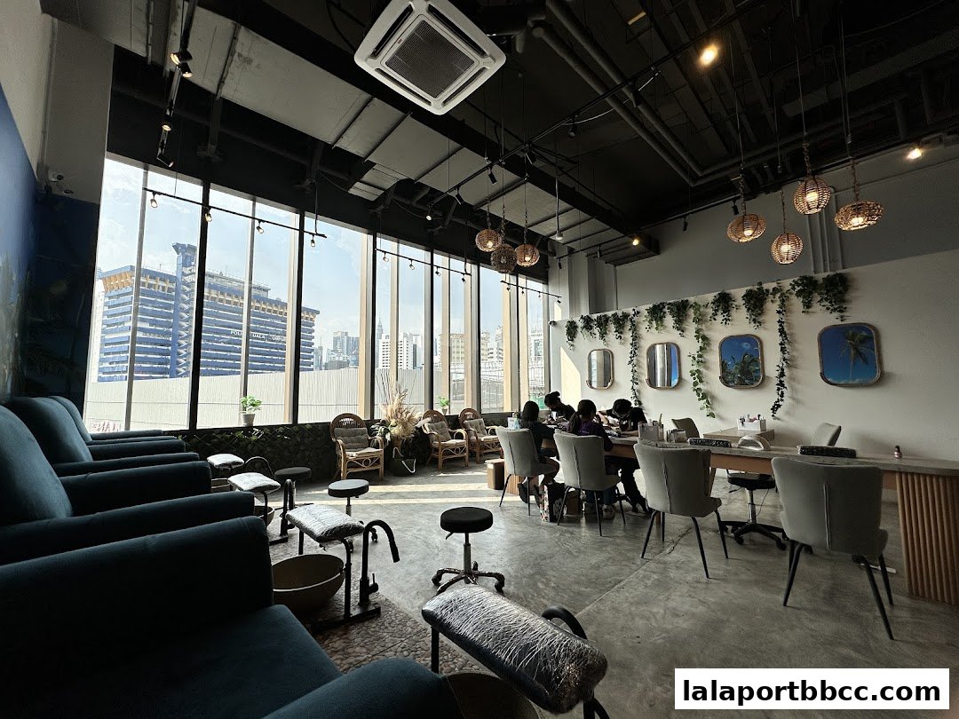 Interior of a modern nail salon with pedicure chairs and manicure stations, featuring large windows with city views.