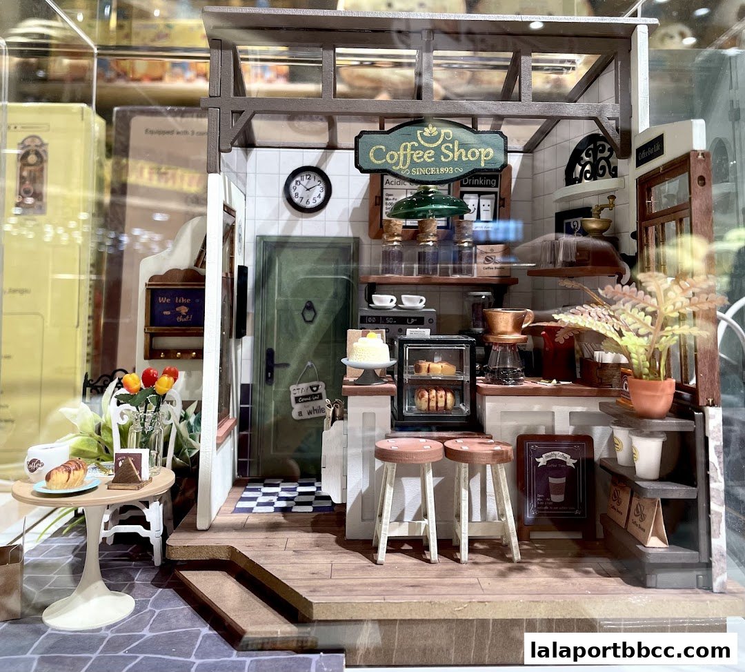 A miniature diorama of a cozy coffee shop interior with a counter, seating, and baked goods.