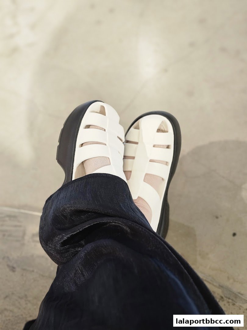A close-up shot of a person wearing white Crocs sandals and dark blue pants.