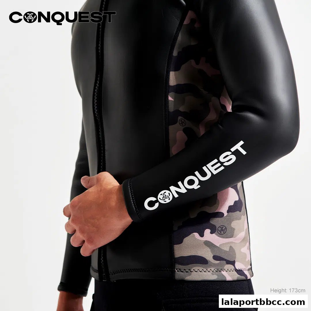 A person wearing a black wetsuit with camouflage panels and the CONQUEST logo.