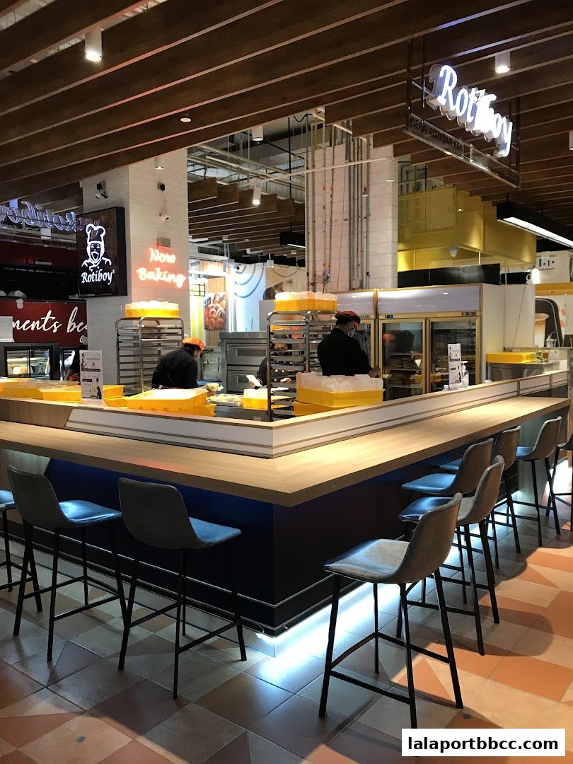 A bakery counter with staff preparing food and bar stools in front.
