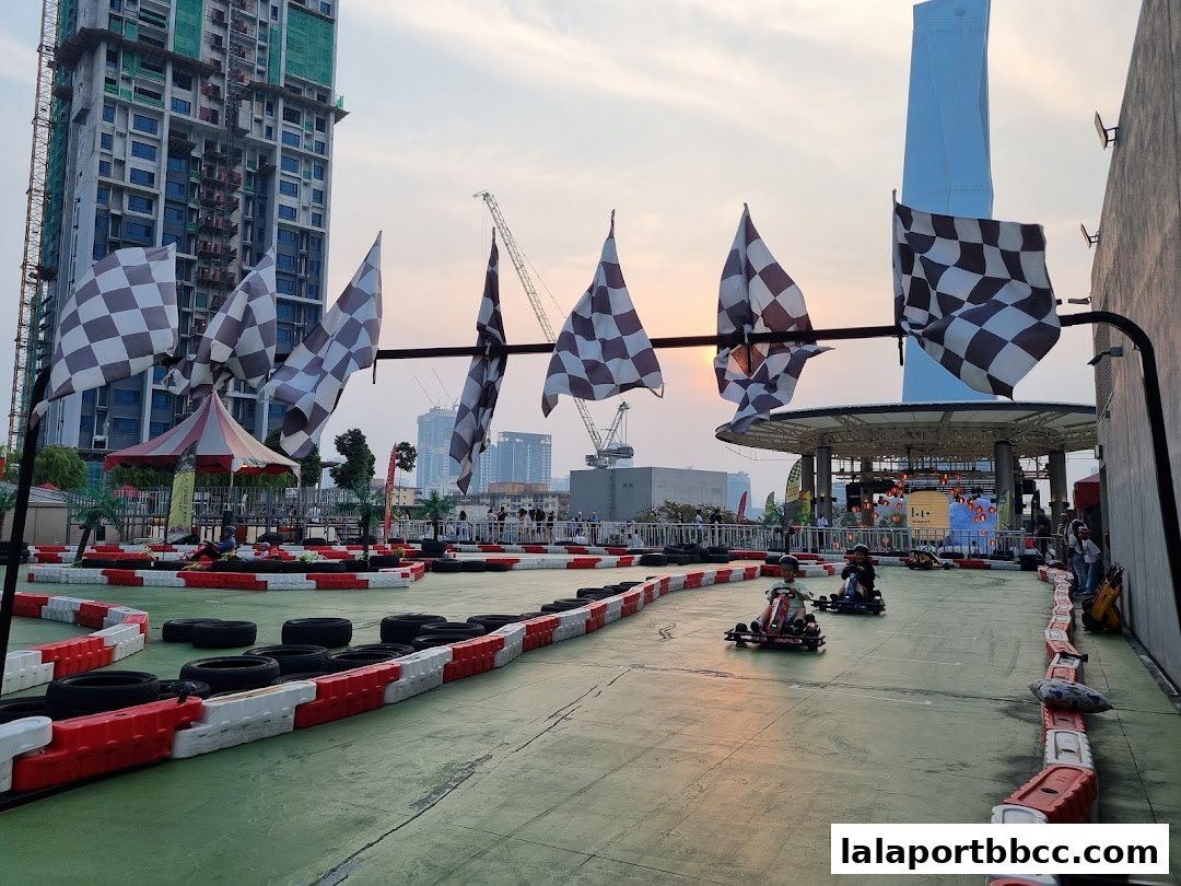 Go-karts racing on an outdoor track with checkered flags and city skyline in the background.