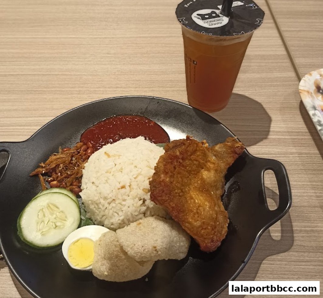 A plate of Nasi Lemak with fried chicken and a drink.